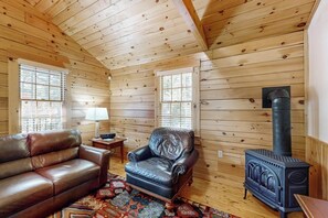 Ein Holzblockhaus-Interieur mit Ledersofa, Ledersessel, einem kleinen Tisch mit Lampe und einem Kaminofen.