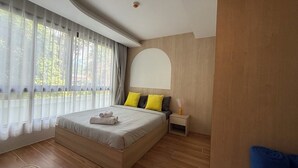 Een moderne slaapkamer met een groot bed, een nachtkastje, een wandboog en een raam met dunne gordijnen.