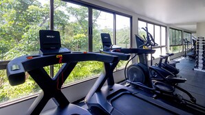 Een sportschool met loopbanden en elliptische machines, grote ramen met uitzicht op groen en diverse gewichten.