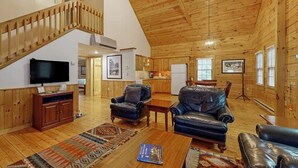 Ein geräumiger Wohnbereich mit Holzboden, einem Fernseher, Ledersofas, einem Esstisch und einer Treppe.