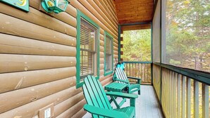 Eine Holzhütte mit Veranda, zwei grüne Adirondack-Stühle und ein Fenster mit Fensterläden.