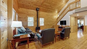 Ein Holzinterieur mit einer Couch, Stühlen, einem Fernseher und einer Treppe.