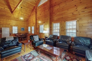 Ein Interieur einer Holzhütte mit Ledersofas, einem Esstisch und einem gemusterten Teppich.