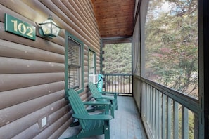 Eine Holzhütte mit Veranda, Hausnummer 102, und grünen Adirondack-Stühlen.