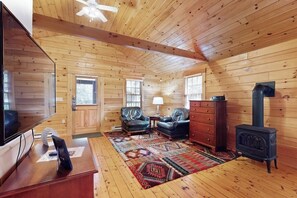 Ein Holzblockhaus-Innenraum mit Fernseher, Ledersesseln, einem Schminktisch, einem Herd und einem gemusterten Teppich.