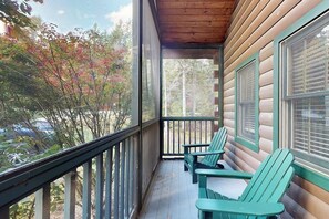 Eine Holzhütte mit Veranda, grünen Adirondack-Stühlen und Blick auf Bäume und ein Auto.