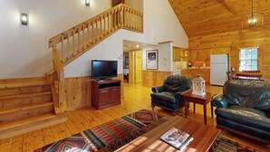 Un interior de madera con una escalera, televisor, sofás de cuero y una zona de cocina.