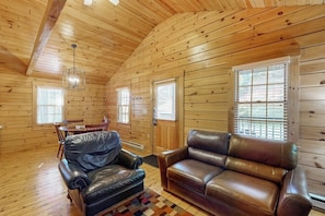 A log cabin interior with a leather sofa, a dining table with chairs, and a chandelier.