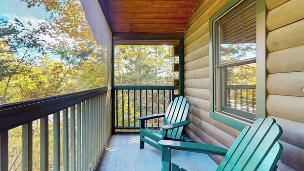 Un porche de madera con dos sillas Adirondack, barandilla y ventana con vista a árboles.