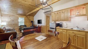 Interior acogedor de una cabaña con una mesa de comedor de madera, un sofá, un televisor y una zona de cocina.
