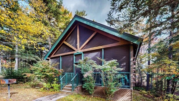A cabin with a steeply pitched roof, a porch with a railing, and a pathway leading to the entrance. - Bobcat Cabin, dog-friendly cabin retreat with full kitchen, outdoor activities (Northport)