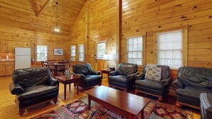 A log cabin interior with a dining area, leather sofas, a coffee table, and a patterned rug. - Bobcat Cabin, dog-friendly cabin retreat with full kitchen, outdoor activities (Northport)