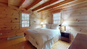 A wooden cabin room with a bed, two bedside lamps, a heater, and a TV. - Bobcat Cabin, dog-friendly cabin retreat with full kitchen, outdoor activities (Northport)