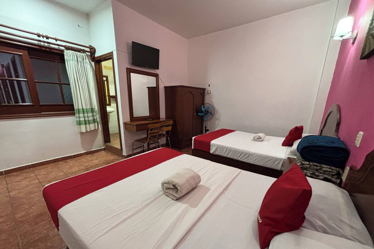 A hotel room with two beds, a desk, a mirror, a TV, and a window with curtains.