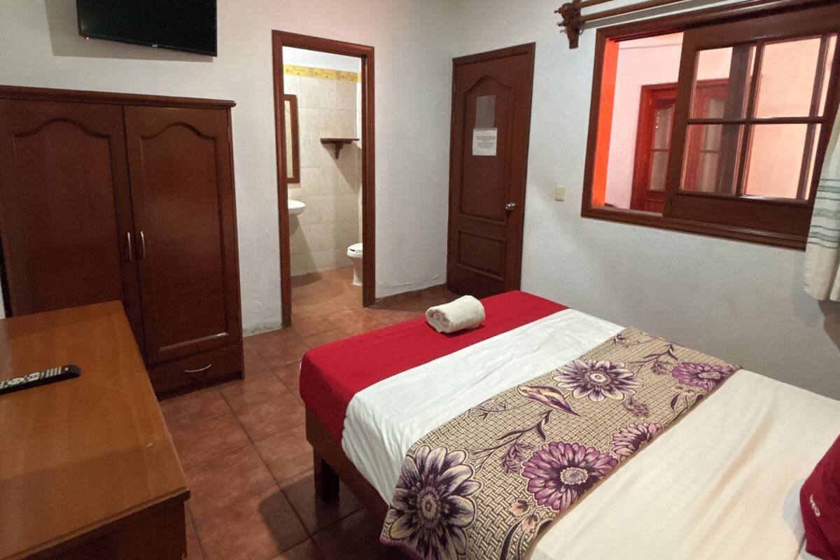 A bedroom with a bed, a wooden wardrobe, a television, and a window.