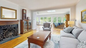 Uma sala de estar espaçosa com lareira, sofá, mesa de centro e uma grande janela com vista para o exterior.