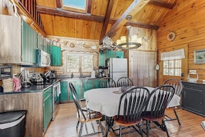 A wooden cabin interior with a kitchen, dining area, and a large window. - Charming riverfront home with cozy interiors, dock, and scenic deck views (Westport Island)