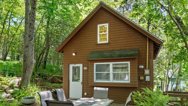 A wooden cabin with a dining table and chairs, surrounded by greenery.