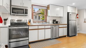 A modern kitchen with stainless steel appliances, white cabinetry, and a window with a view of a house.