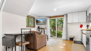 A compact living space with a kitchenette, a sofa, a TV, and a view of greenery.