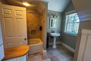 A bathroom with a bathtub, shower, sink, and window. - Charming coastal cottage with deck, grill, firepit, and jetted tub (Trevett)