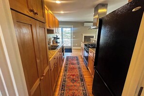 A kitchen with wooden cabinets, a black refrigerator, and a patterned rug. - Charming coastal cottage with deck, grill, firepit, and jetted tub (Trevett)