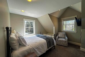 A bedroom with a bed, a chair, two windows, and a sloped ceiling. - Charming coastal cottage with deck, grill, firepit, and jetted tub (Trevett)