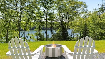 Deux fauteuils Adirondack sont placés face à un foyer extérieur, avec un lac et des arbres en arrière-plan.