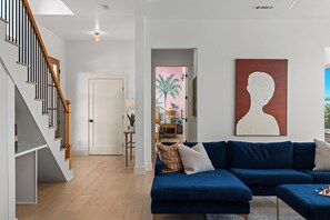 Ein modernes Wohnzimmer mit einem blauen Modulsystem-Sofa, einer Treppe mit Holzwerteln und einem großen abstrakten Gemälde an der Wand.