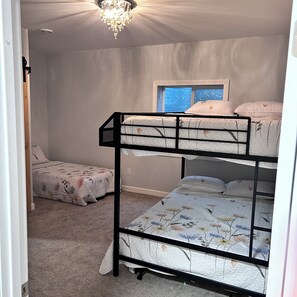 A bunk bed room with a window, carpeted floor, and a chandelier. - Spacious 5-bed 3 bath house in beautiful Nauvoo with 1 acre fully stocked pond (Nauvoo)