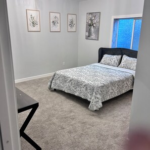 Un dormitorio con una cama, piso alfombrado y tres cuadros con motivos florales en la pared.