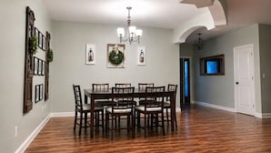 A dining room with a wooden table and chairs, a chandelier, framed pictures, and a wreath on the wall.