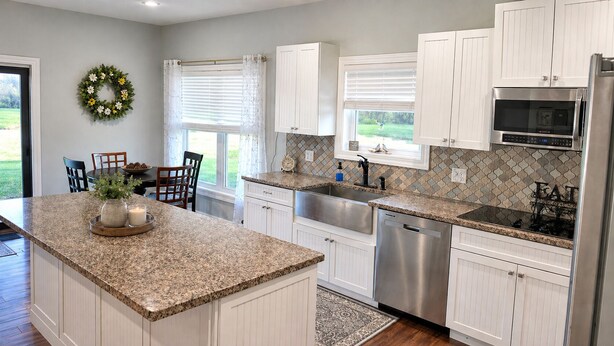 A kitchen with white cabinets, a granite countertop, stainless steel appliances, and a view of the outdoors.