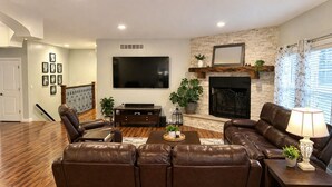 A living room with a sectional sofa, a flat-screen TV, a fireplace, and a staircase.