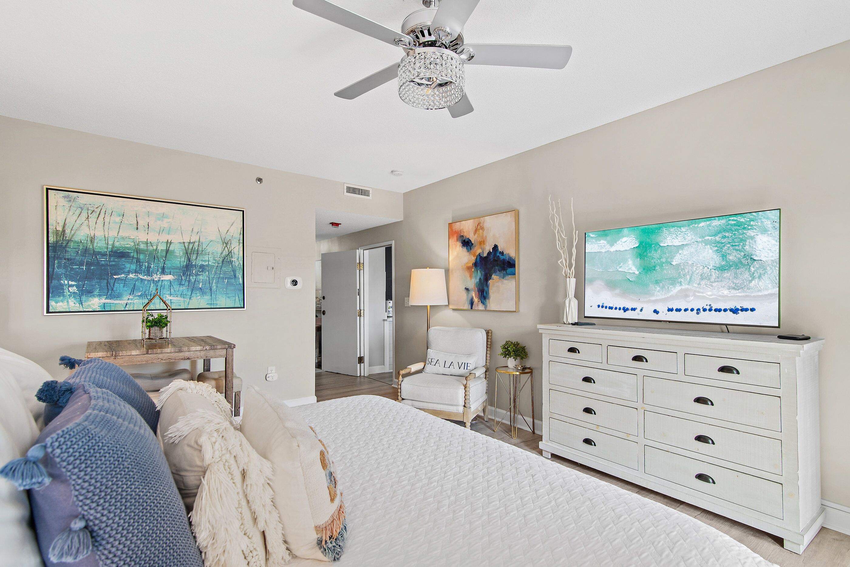 A bedroom with a bed, a TV, a ceiling fan, and artwork on the walls.