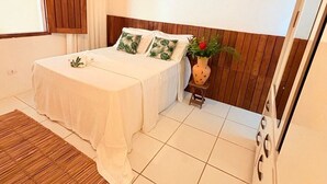 A bedroom with a bed, wooden headboard, white bedding, a small table with a vase, and a wooden floor. - Beautiful Leisure House (Trancoso)