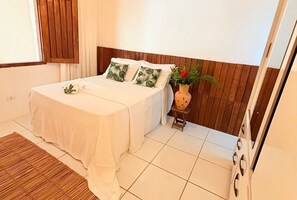 A bedroom with a bed, wooden headboard, white bedding, a small table with a vase, and a wooden floor. - Beautiful Leisure House (Trancoso)