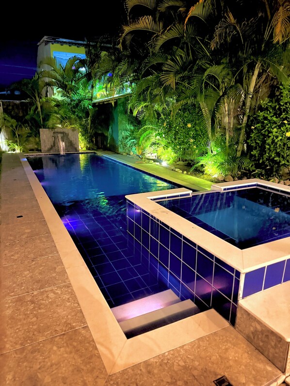 A swimming pool with a tiled edge, surrounded by lush greenery and a stone wall. - Beautiful Leisure House (Trancoso)
