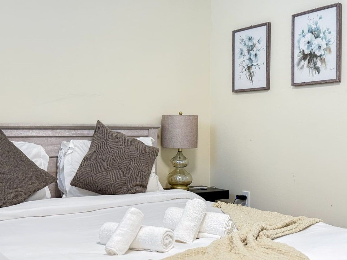 A neatly made bed with pillows, a lamp, and two framed artworks on the wall.