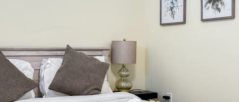 A neatly made bed with pillows, a lamp, and two framed artworks on the wall.