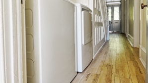 Un couloir avec un réfrigérateur blanc et un four blanc, un plancher en bois et des portes blanches.