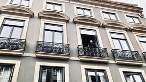 Un immeuble à plusieurs étages, doté de balcons et de grandes fenêtres, sur lequel se trouve une personne, debout sur l’un des balcons.