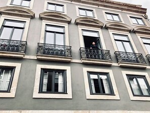 Ein mehrstöckiges Gebäude mit Balkonen und großen Fenstern, auf einem Balkon steht eine Person.