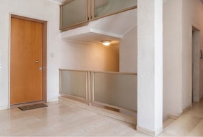 Un couloir avec une porte en bois, un balcon doté d’une balustrade et un luminaire fixé au mur.