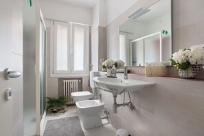 Une salle de bain moderne avec un lavabo blanc, un bidet et des toilettes, un grand miroir et un radiateur.