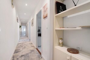 Un couloir doté d’un sol recouvert de moquette, de murs blancs et d’étagères où sont disposés divers objets.