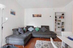 Een woonkamer met een grijze modulaire bank, een witte boekenkast en twee aan de muur bevestigde schilderijen.