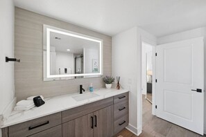 Une salle de bain avec un grand miroir, un lavabo, un porte-serviettes et une plante en pot.