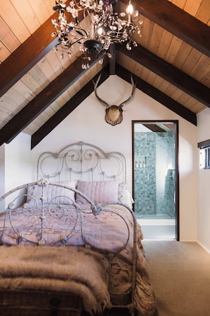 Un dormitorio con techo abovedado, una cama con cabecera decorativa, una araña y una decoración con cabeza de venado.