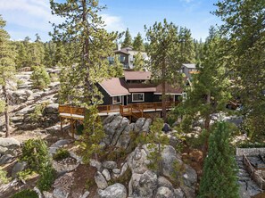 Una cabaña con terraza de madera, rodeada de grandes rocas y pinos.